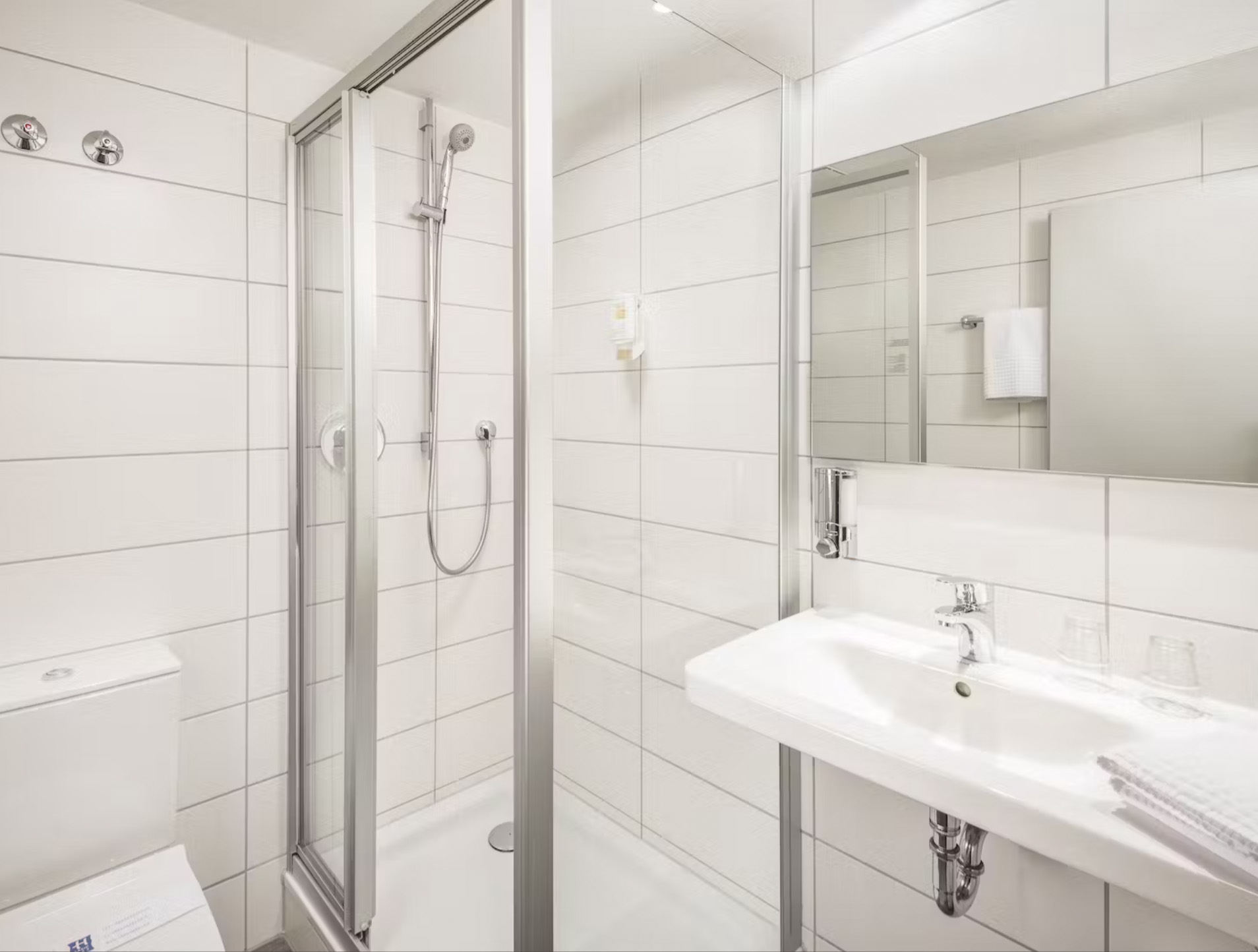 Helles Badezimmer mit Dusche, Waschbecken, Spiegel und Toilette.