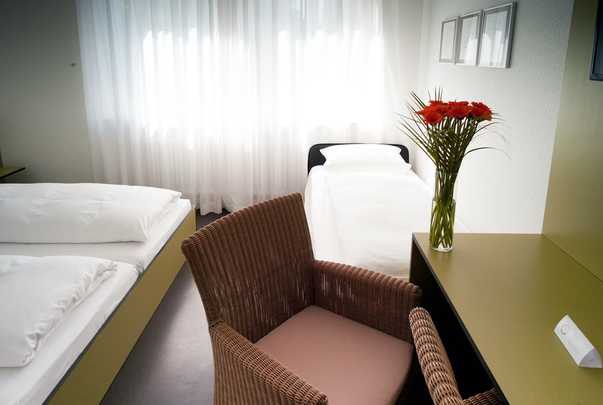 Elegantes Doppelzimmer mit Zustellbett, Rosenvase und Holzhockern
