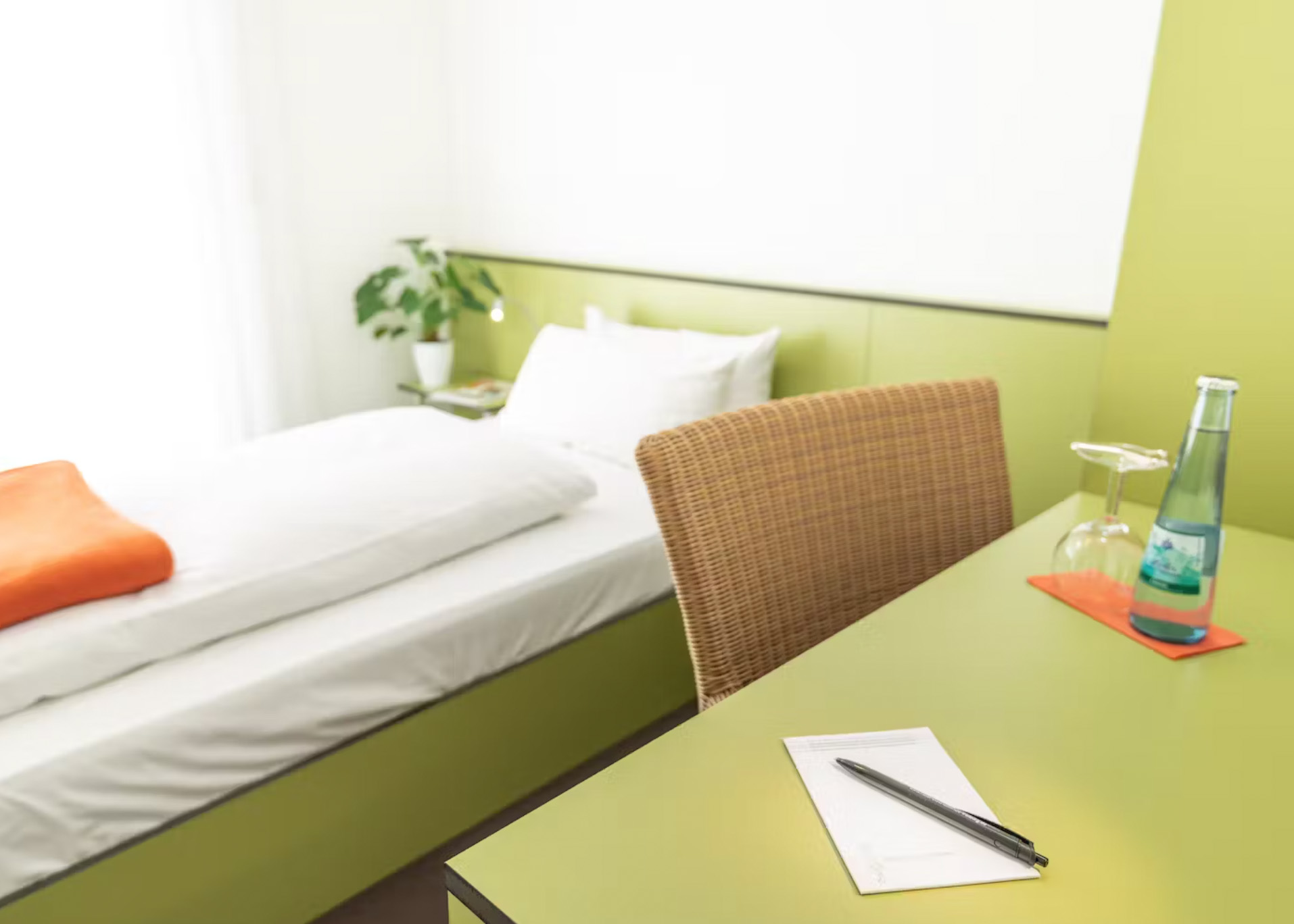 Einzelzimmer mit Bett, Schreibtisch, Schreibblock und Blick auf Sessel und Schrank