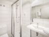 Helles Badezimmer mit Dusche, Waschbecken, Spiegel und Toilette.