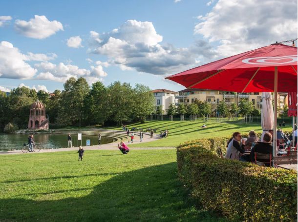 Blick vom Lago Restaurant auf den Seepark mit Kindern, Radfahrern und Besuchern