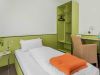Modernes Einzelzimmer mit Bett, Schreibtisch, Korbsessel und grünem Schrank