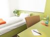 Einzelzimmer mit Bett, Schreibtisch, Schreibblock und Blick auf Sessel und Schrank
