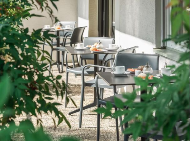 Hotel-Außenansicht mit Tischen, Kaffee, Brötchen und Pflanzen